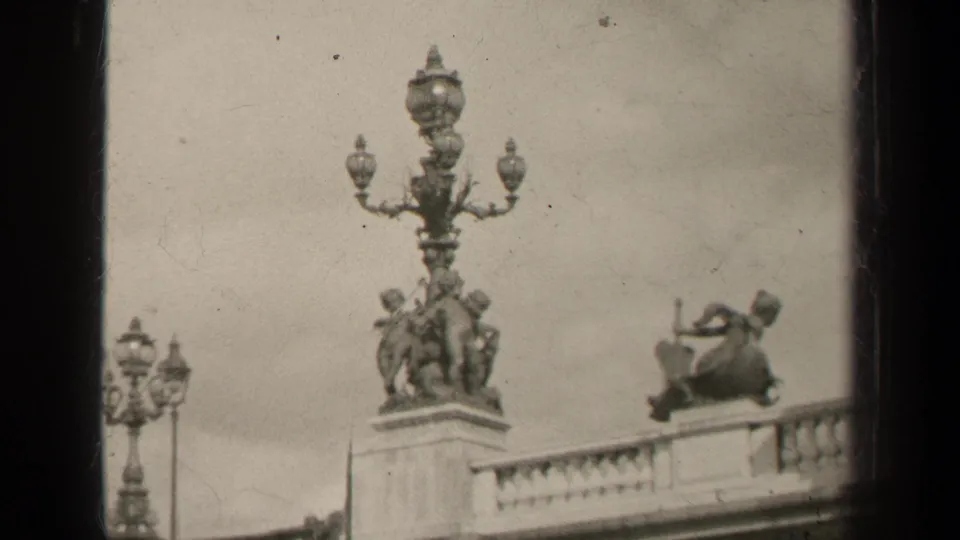 1947 Paris frame looking up at ornate bridge lampposts, sculptural figures, and a stone balustrade against a pale sky.