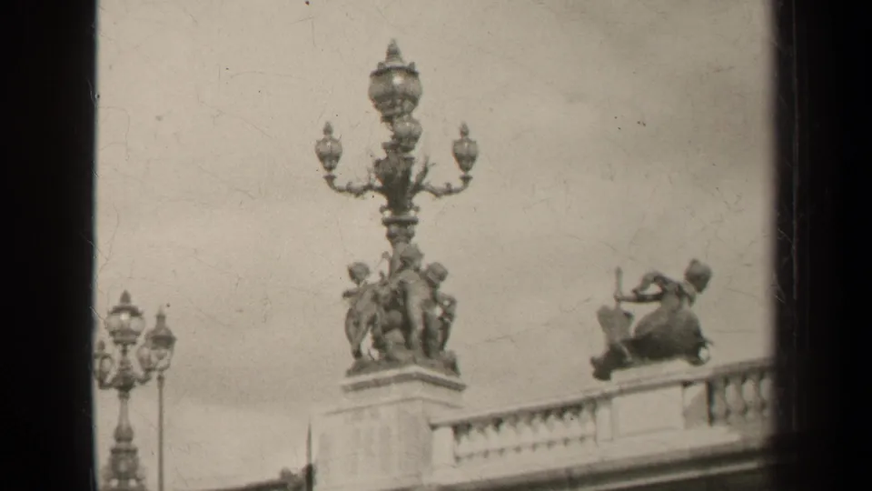 1947 Paris 8mm frame showing an ornate multi-globe lamp, classical sculptural figures, and a balcony balustrade.