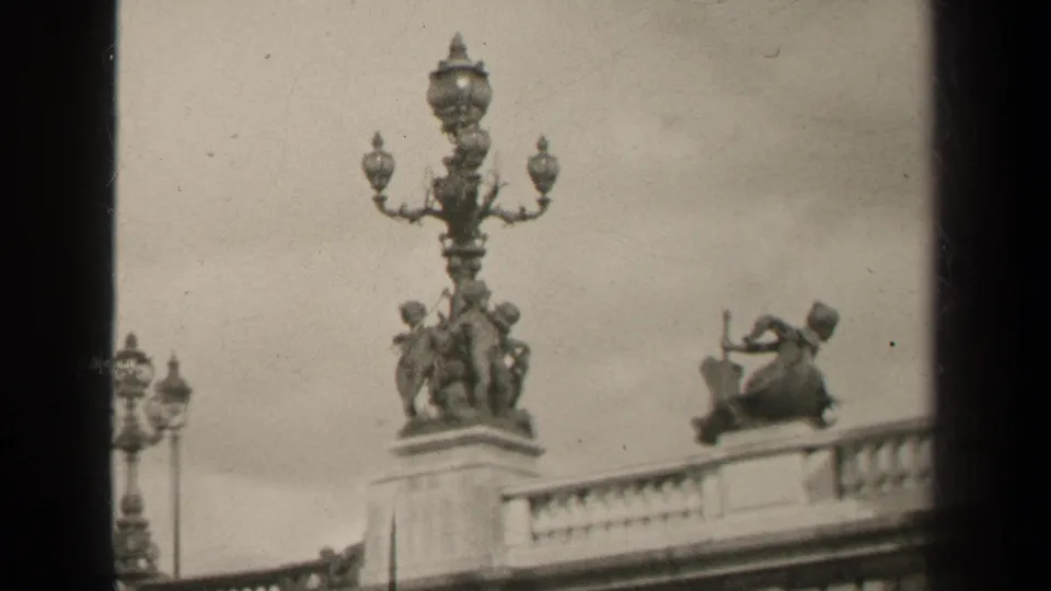 1947 Paris home-movie frame showing ornate balcony sculpture, multi-globe lamp details, and visible 8mm frame edges.