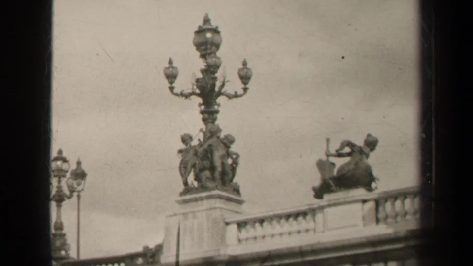 1947 Paris home-movie frame showing a decorative lamppost, stone figures, and bridge balustrade in soft black-and-white focus.