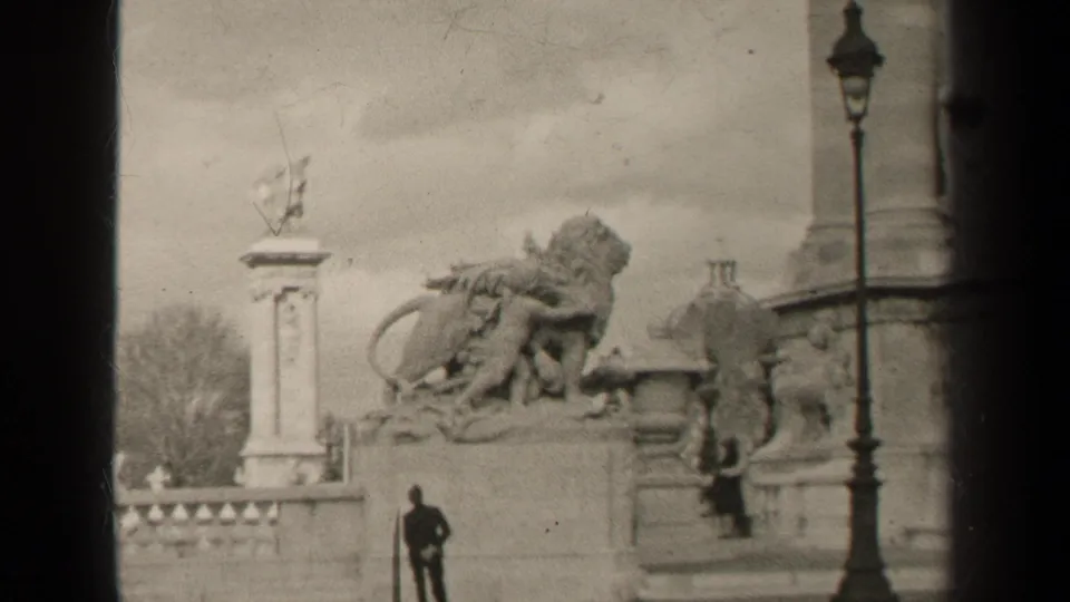 1947 Paris frame with a large stone lion group, balustrade, right-side lamppost, and a distant man standing below.