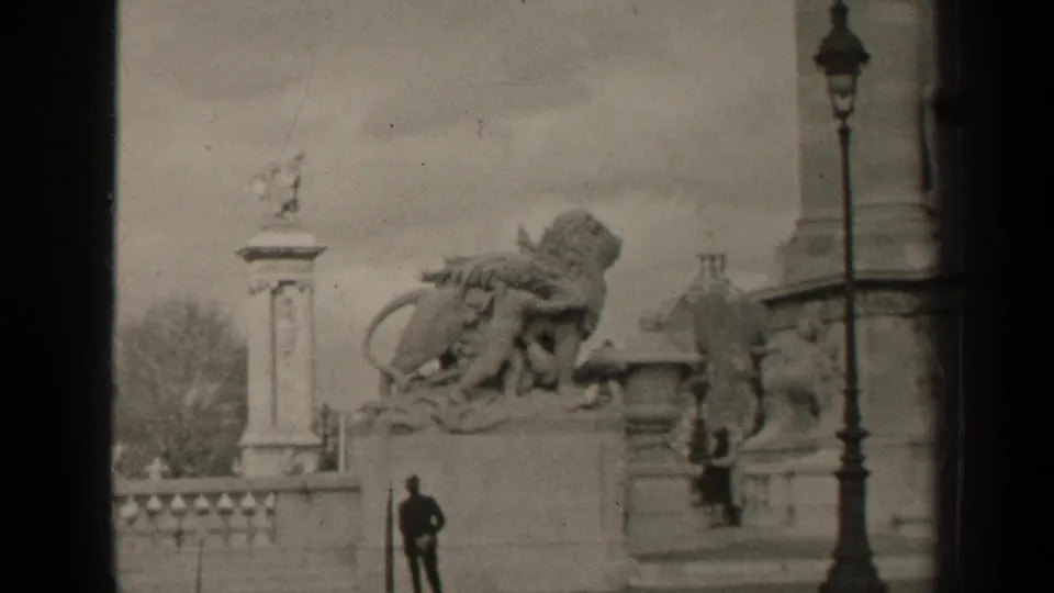 1947 Paris home-movie still with lion sculpture, lamppost, balustrade, trees, and a distant man in period clothing.