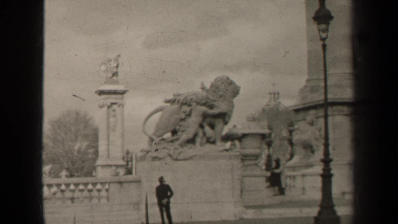 Stone monument with lion sculpture, balustrade, street lamp and a person standing in the square.
