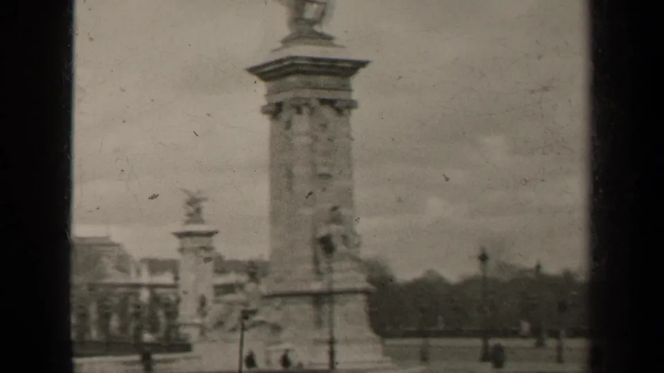 1947 Paris frame with a tall monument column, lion sculpture at its base, a smaller monument in the distance and pedestrians crossing the square.