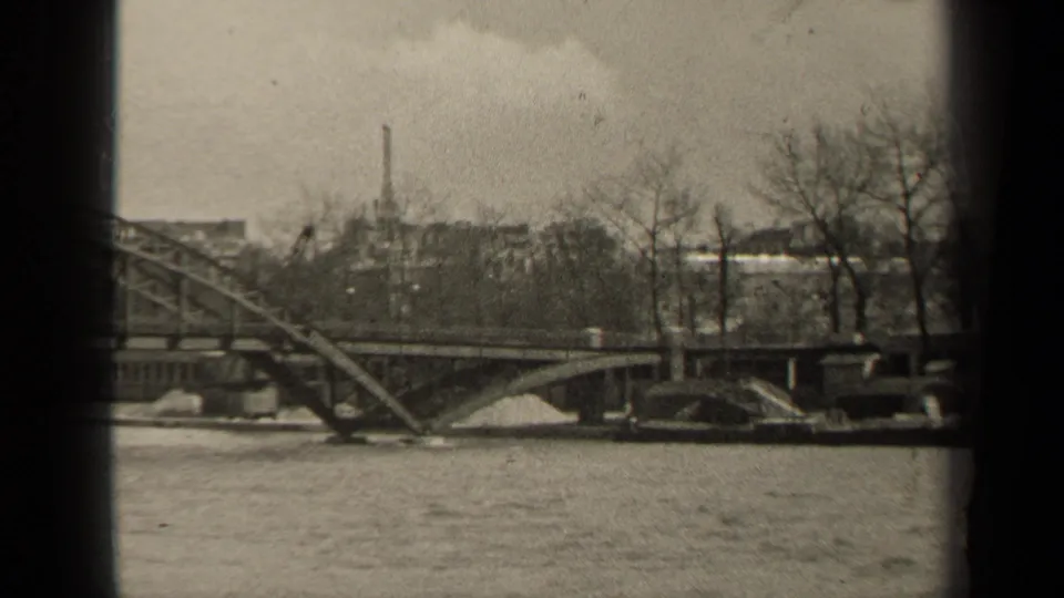 1947 Paris home-movie still with the bridge structure, river surface, bare trees, and distant buildings framed by dark film edges.