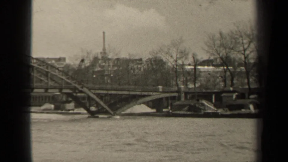 1947 Paris riverfront frame showing water in the foreground, a steel bridge, bare trees, and soft urban forms behind it.