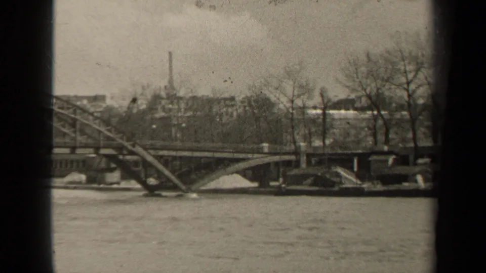 1947 Paris river view with bridge approach, stone embankment, leafless trees, background buildings, and soft 8mm grain.