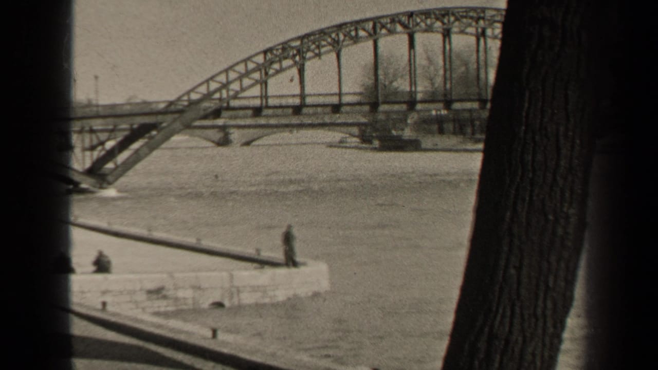1947 Paris river view framed by trees, showing a steel truss bridge, high water, and distant people watching from a stone embankment.