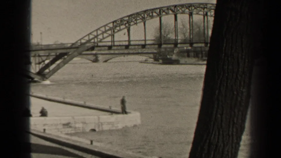 1947 Paris river view framed by trees, showing a steel truss bridge, high water, and distant people watching from a stone embankment.