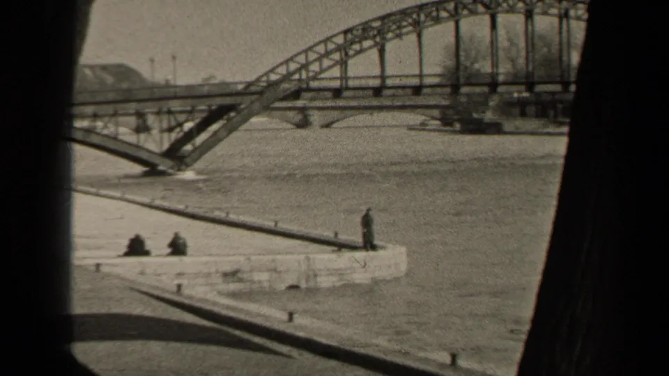 Mid-century Paris 8mm frame with a steel bridge over high water and several distant observers on the stone riverside embankment.