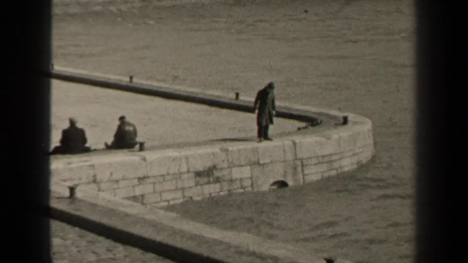 1947 Paris riverside frame showing several people on a stone platform, including seated figures and one standing near the water.