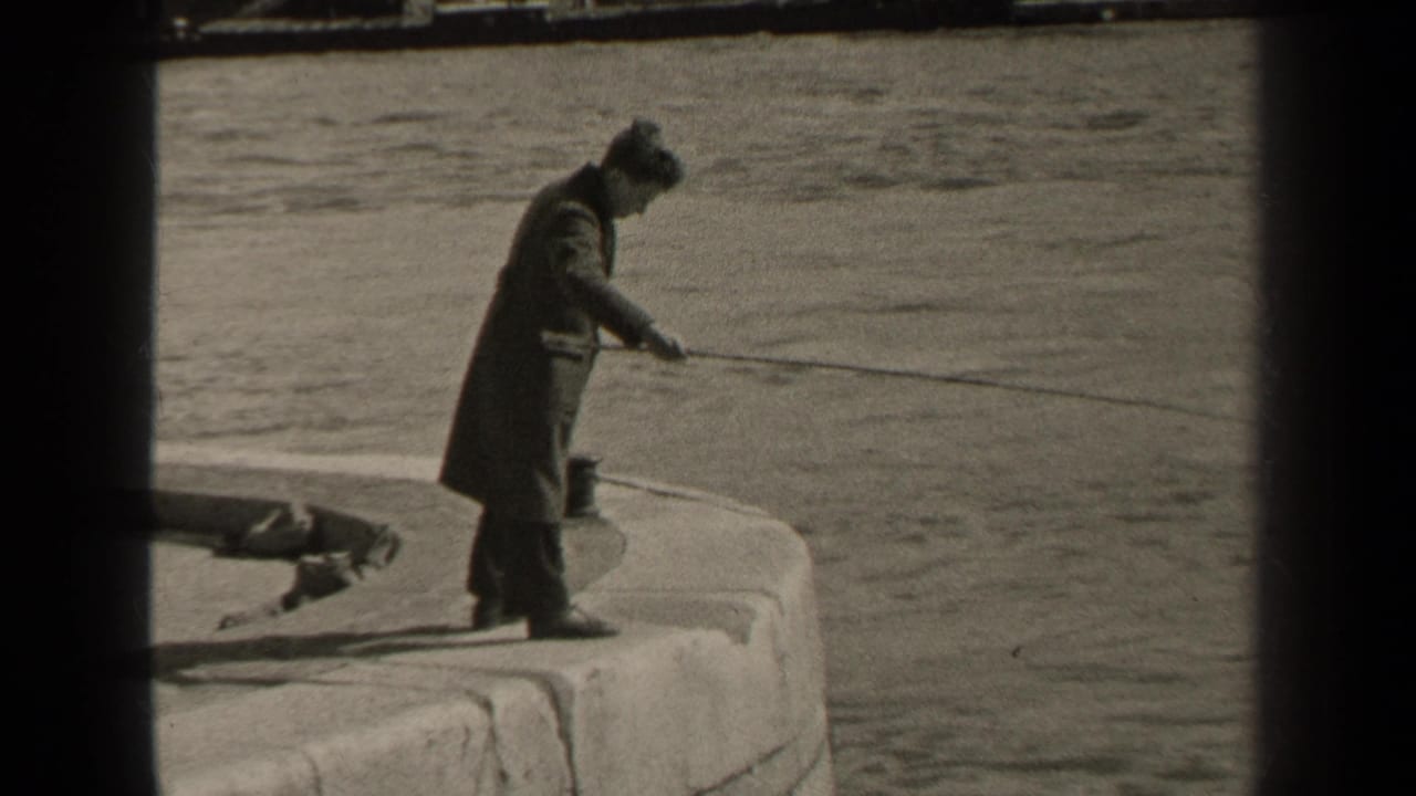 1947 Paris frame of a man in a long coat and hat fishing from the edge of a curved stone pier.