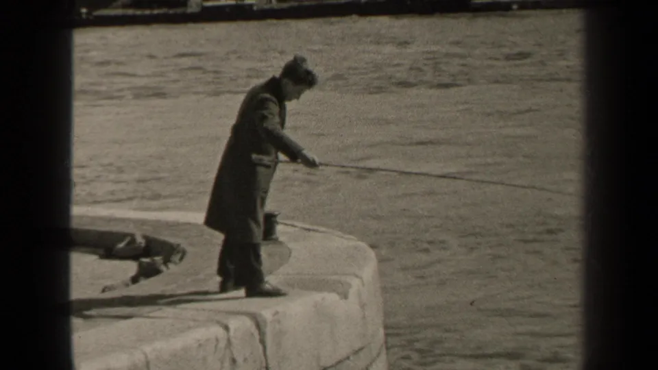 1947 Paris frame of a man in a long coat and hat fishing from the edge of a curved stone pier.