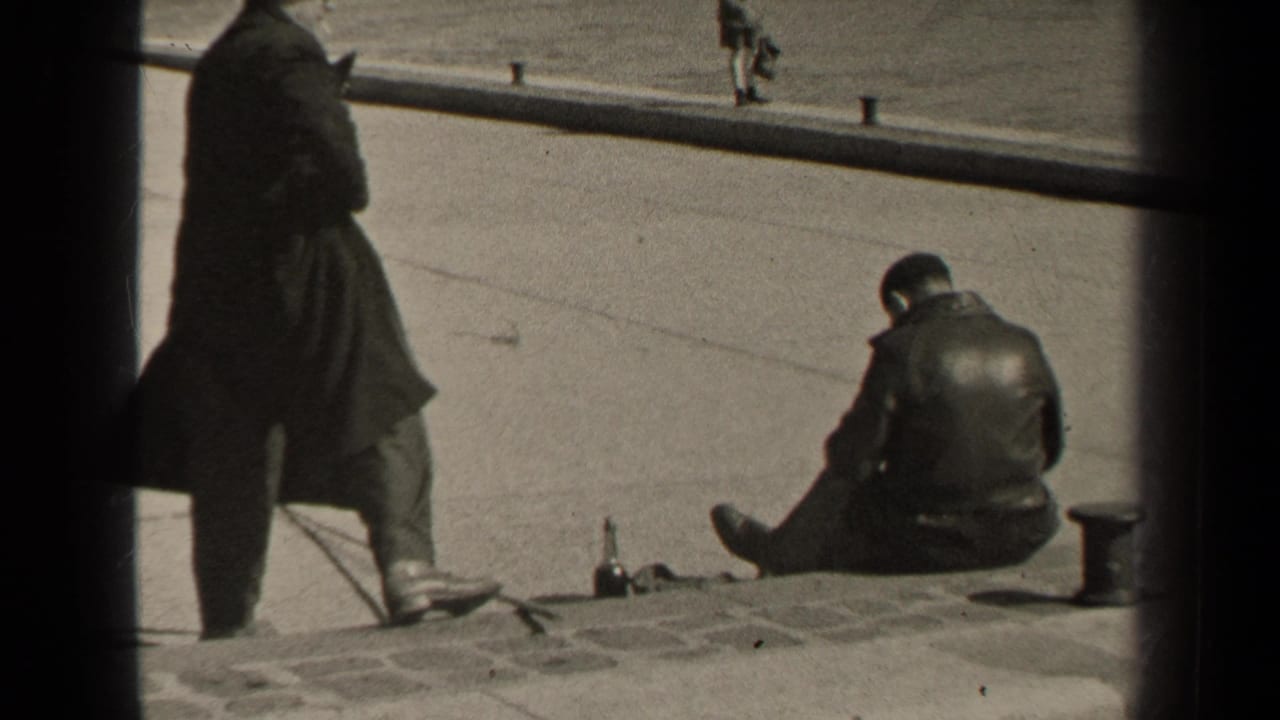 1947 Paris street frame with a standing man partly in shadow and another man seated on the curb near a bottle.