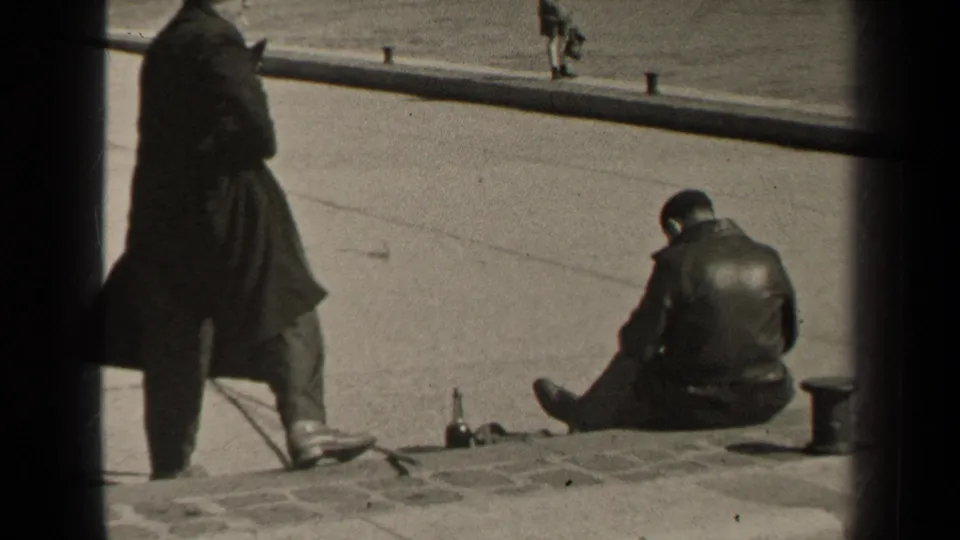 1947 Paris street frame with a standing man partly in shadow and another man seated on the curb near a bottle.