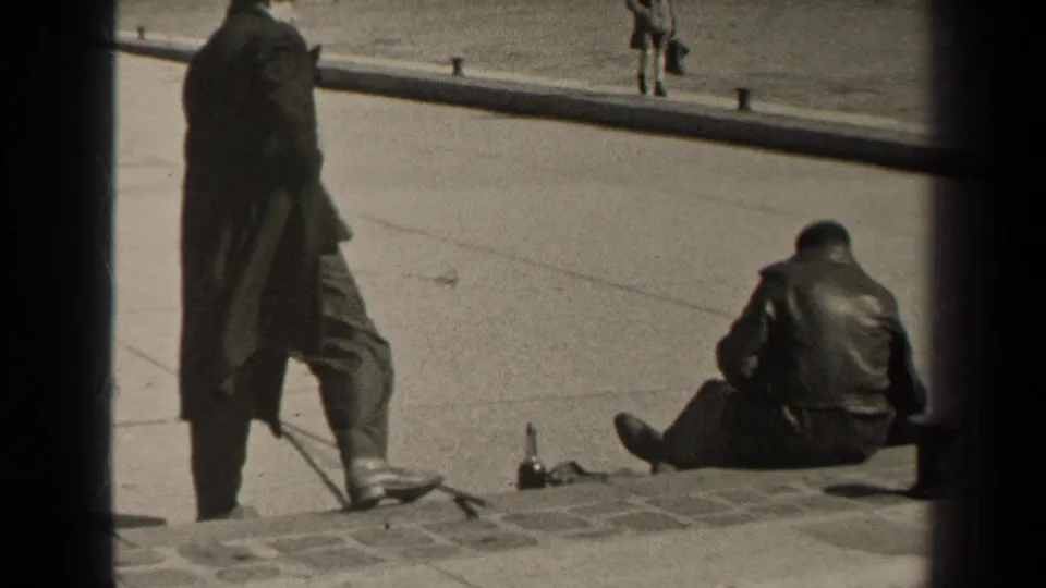 1947 Paris curbside frame showing a seated man in a dark jacket, a standing figure, and open pavement beyond.