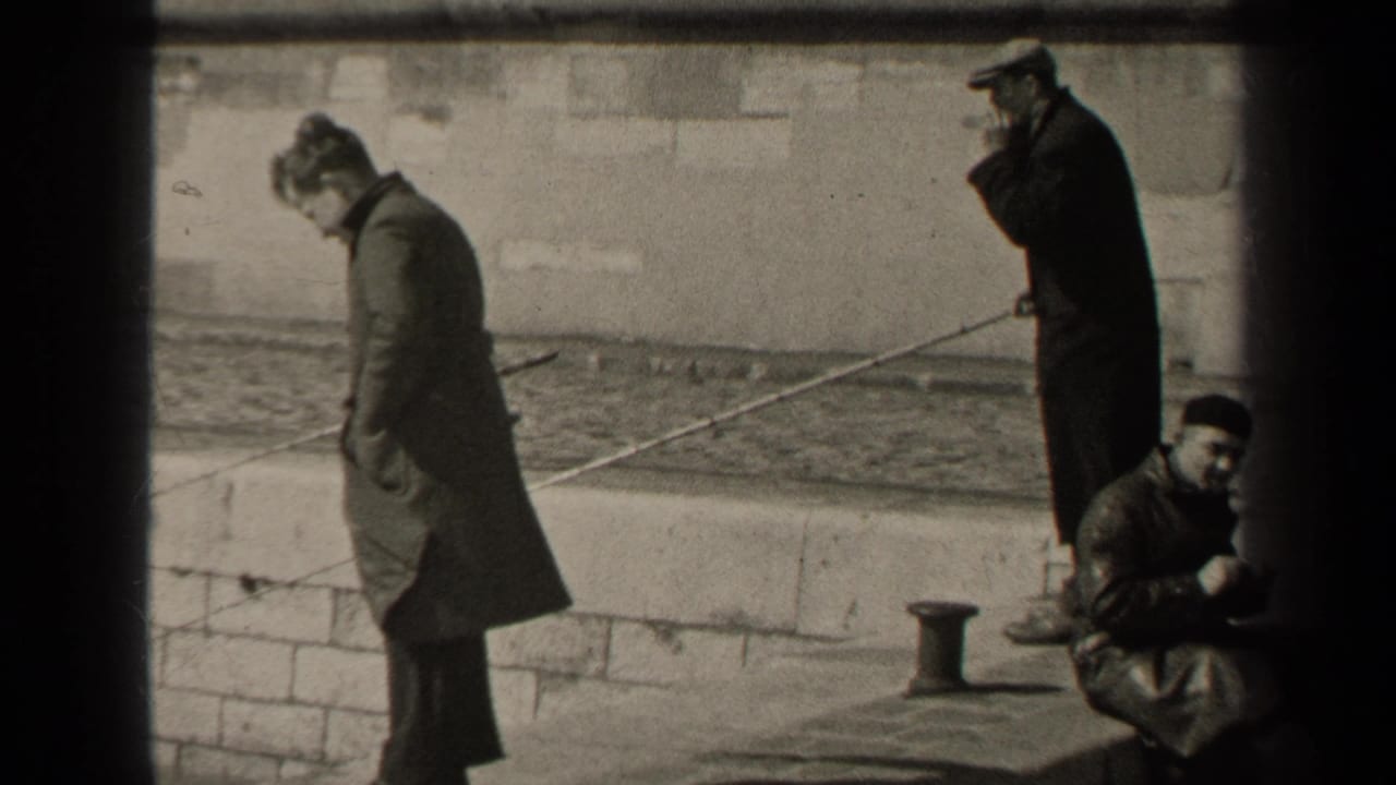 1947 Paris 8mm frame showing men in coats on a stone waterfront wall, with fishing rods, water and a seated man nearby.