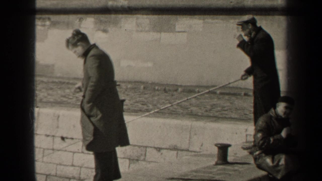Black-and-white 1947 Paris frame of men fishing from a stone embankment, one man smoking while holding a rod.