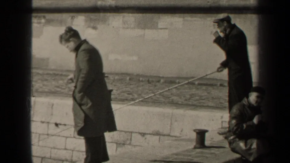 Black-and-white 1947 Paris frame of men fishing from a stone embankment, one man smoking while holding a rod.