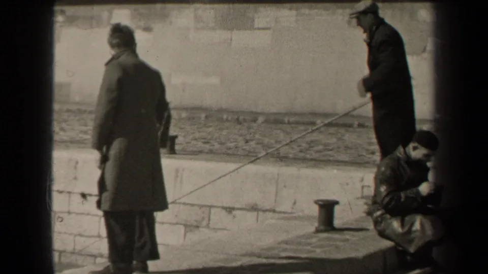 1947 Paris riverside frame with two men using long fishing rods and a third adult facing the water near a stone wall.