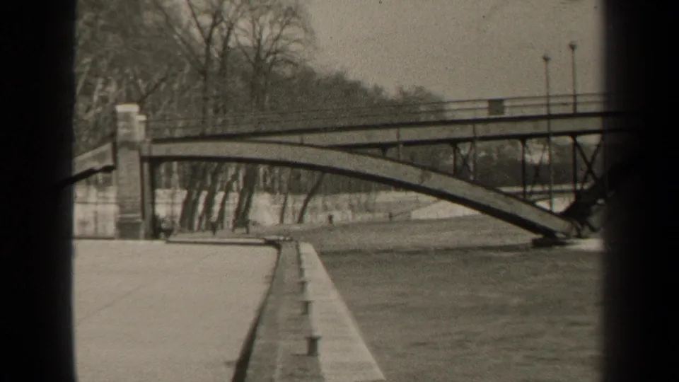 1947 Paris home-movie view of an arched bridge crossing a river, with bare trees along the bank and dark foreground framing.