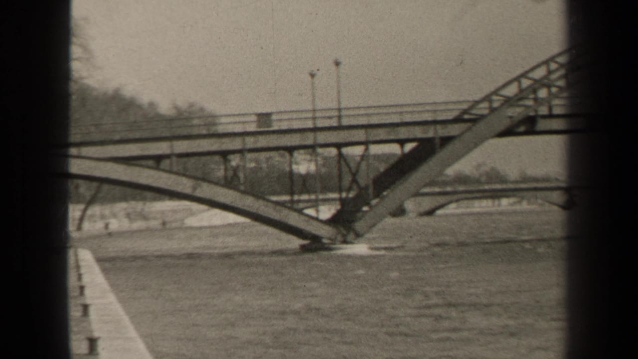 1947 Paris view of a metal arched bridge span over a broad river, with lamps along the deck and another bridge faintly beyond.