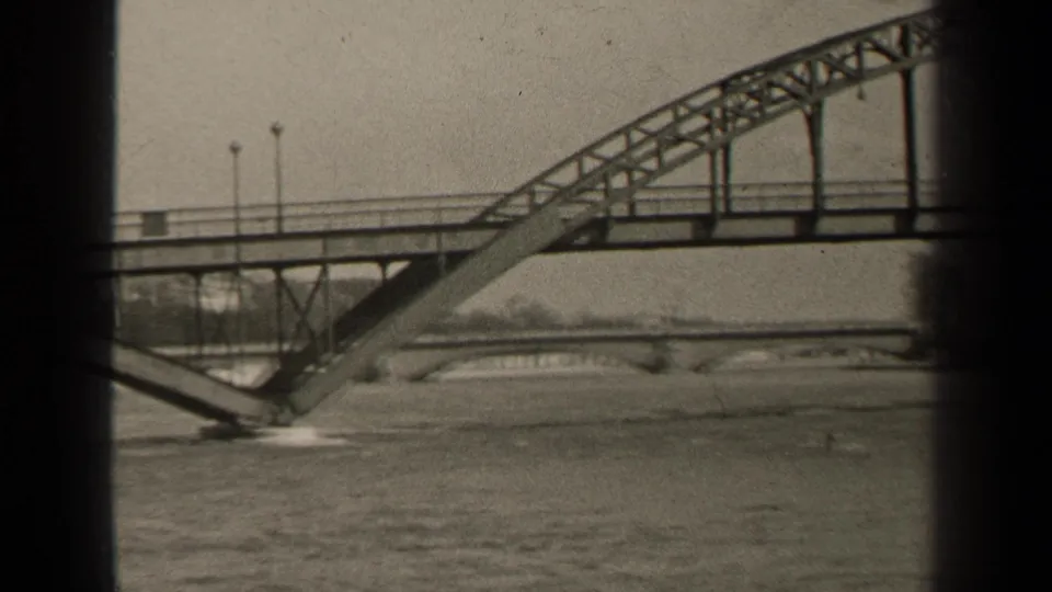 1947 Paris home-movie frame showing the bridge arch, diagonal support, railing, and river below in soft black-and-white 8mm texture.