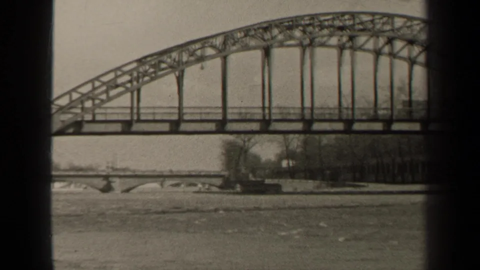 1947 Paris home-movie frame showing a steel arch bridge over a wide river, with bare riverside trees and dark film edges.