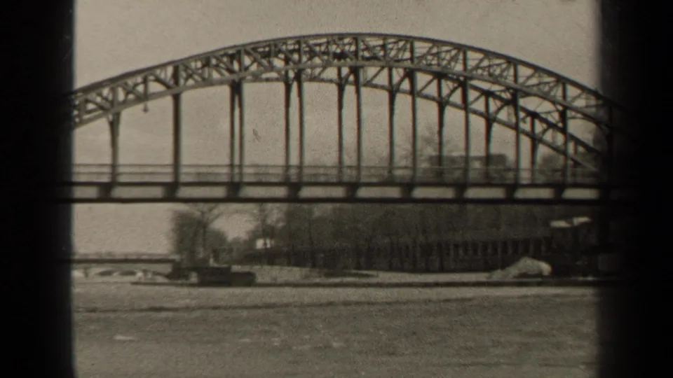 1947 Paris frame with the bridge span centered over the river, showing its arched truss and a quiet tree-lined bank.