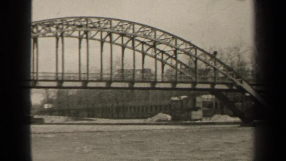 1947 Paris home-movie view of the steel bridge arch, vertical supports, and far riverbank structures beneath the span.