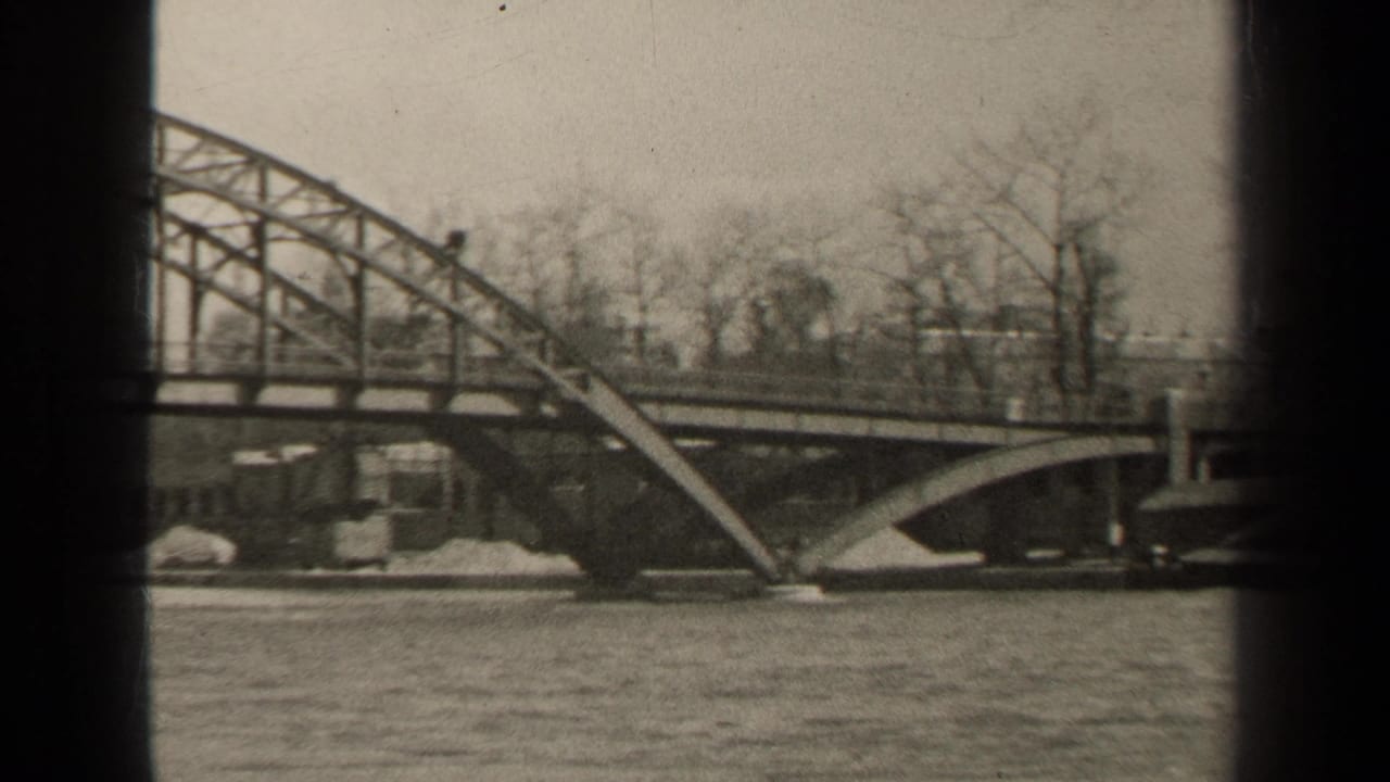 River flowing past a large arched bridge with bare trees behind it.