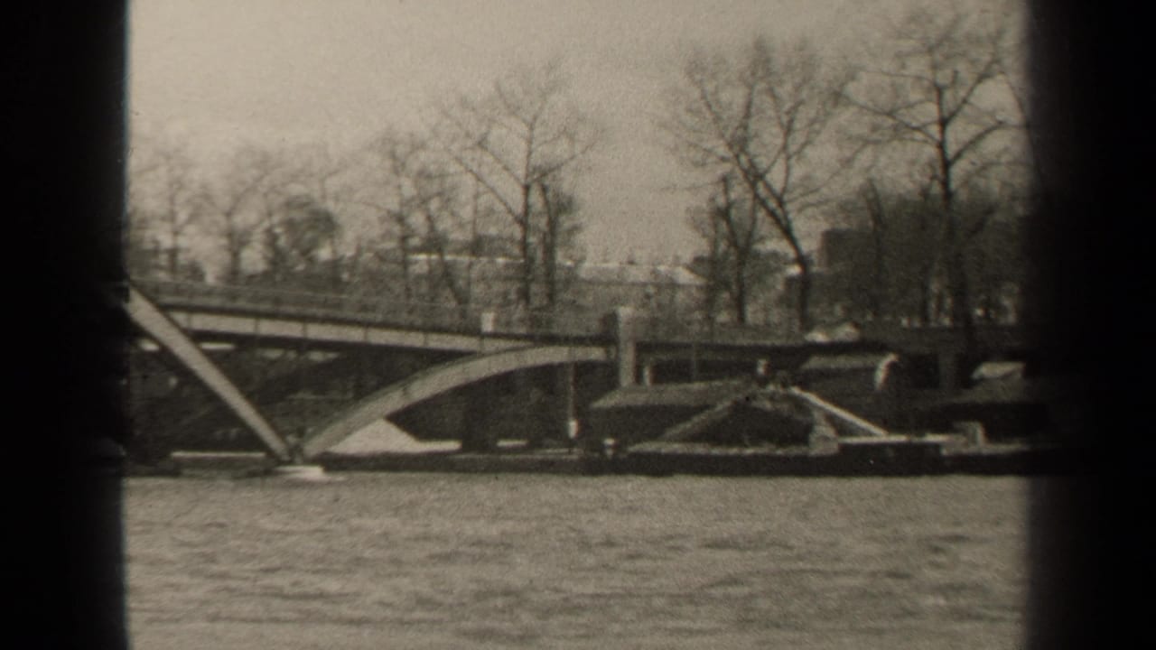 Black-and-white 1947 Paris waterfront frame showing a bridge span, bare trees, embankment details, and moving river water.