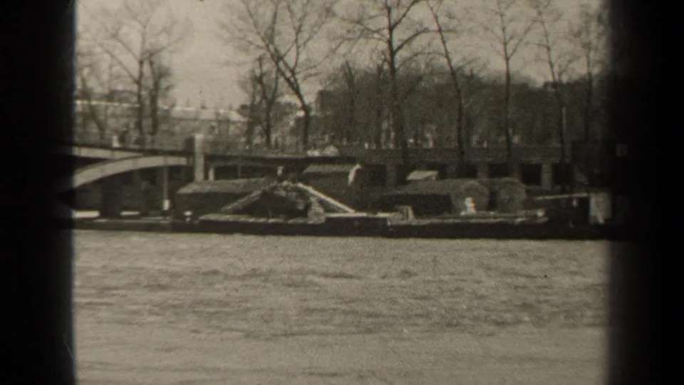 Black-and-white Paris riverbank view from 1947 with bridge edge, winter trees, stone embankment, and swift water in the foreground.