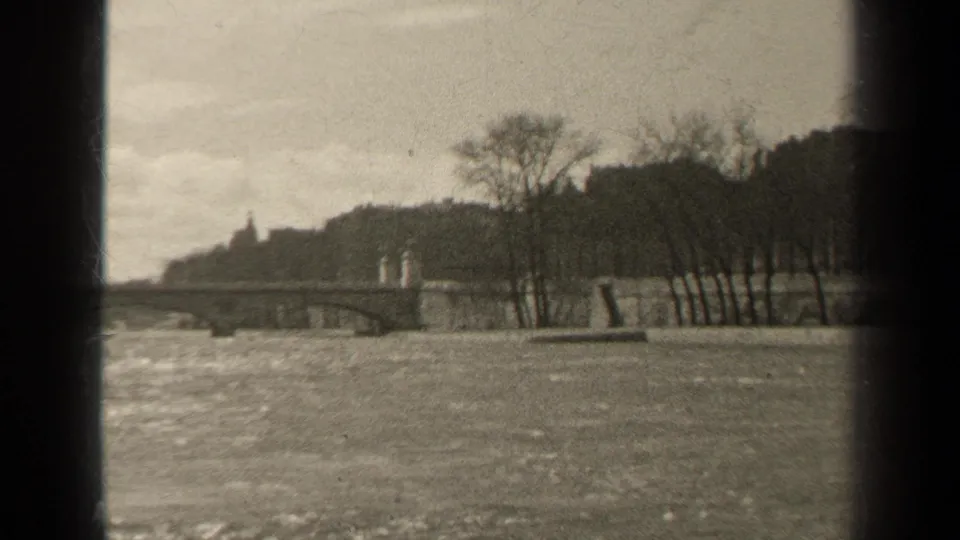 Black-and-white 1947 Paris river scene looking toward a low bridge, bare trees, choppy water, and a shadowed riverside slope.