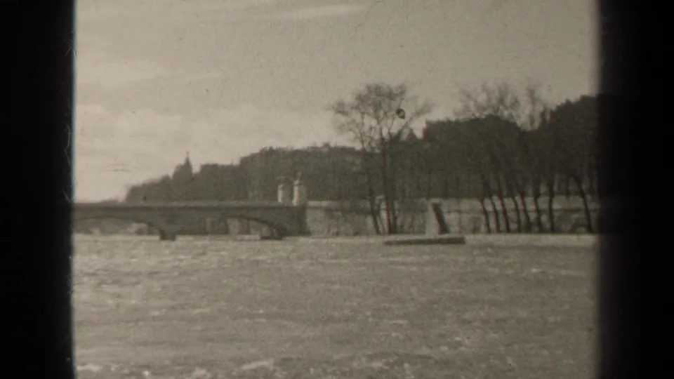 1947 Paris home-movie frame showing a wide river, low bridge, bare trees, and a distant embankment.