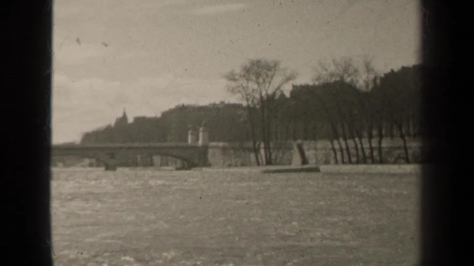 1947 Paris river view with a bridge, winter-bare trees, stone embankment, and visible 8mm frame edge.