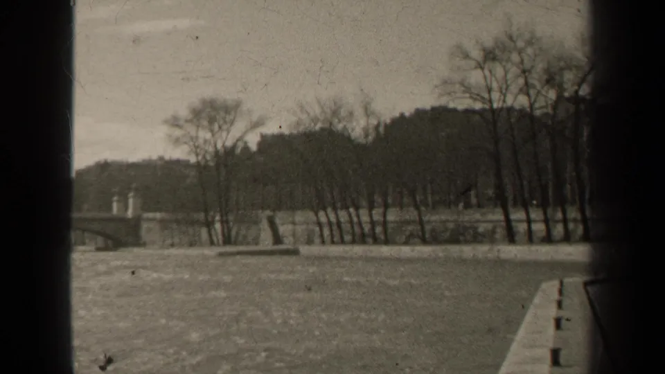 1947 Paris river frame showing a bridge, bare trees, stone bank, and the edge of a boat or dock at lower right.