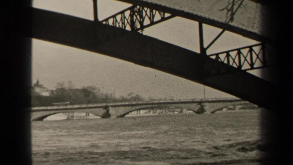 1947 Paris river scene with a prominent steel bridge truss in the foreground and a stone arch bridge beyond.