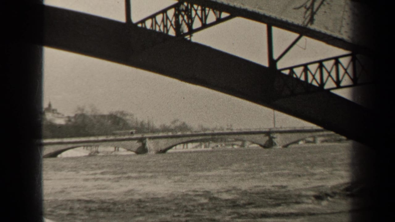 1947 Paris home-movie frame looking from beneath a metal truss bridge across rapid river water toward a distant arched bridge.