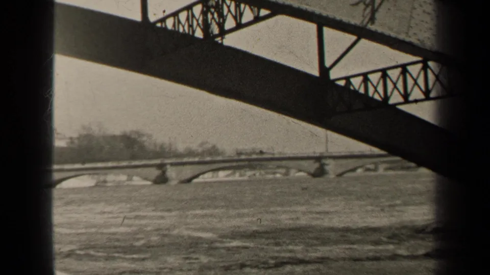Black-and-white Paris river view from 1947, framed by a bridge underside with fast water and distant arched bridge spans.
