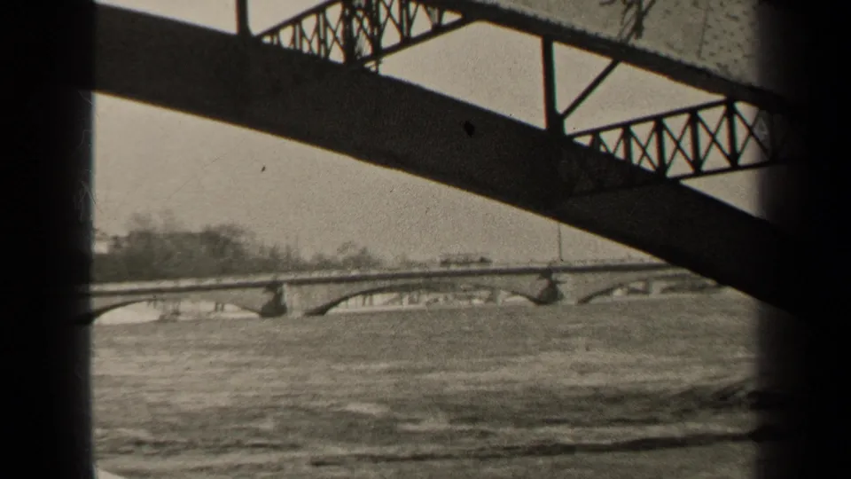 1947 Paris river view with arched bridge spans, flowing water, and dark structural framing in black-and-white 8mm footage.
