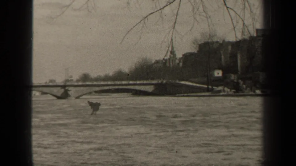 1947 Paris home-movie view of water beneath a bridge, with bare branches and riverside buildings softened by film grain.