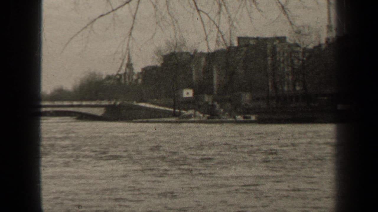 1947 Paris home-movie frame showing a broad river, low bridge, bare branches, and soft city buildings beyond the water.