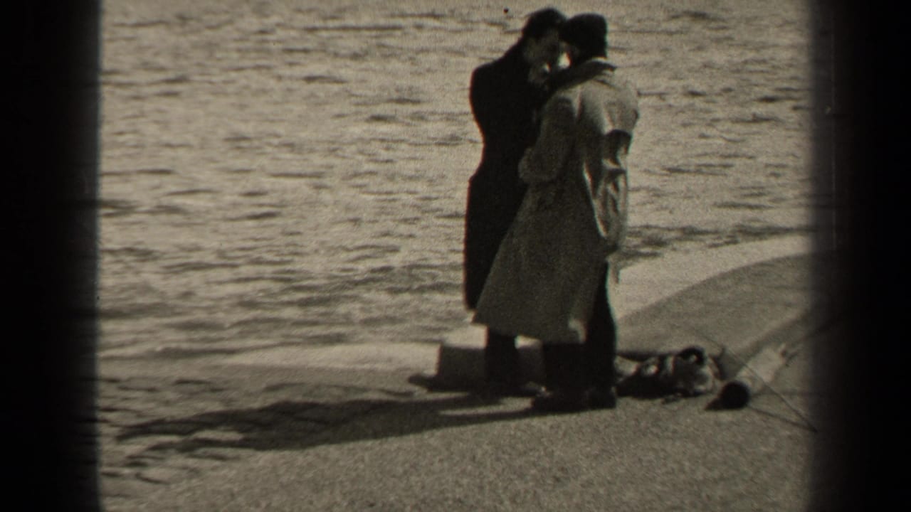 Two men remain close together on a paved edge beside the water, with fishing items near their feet.