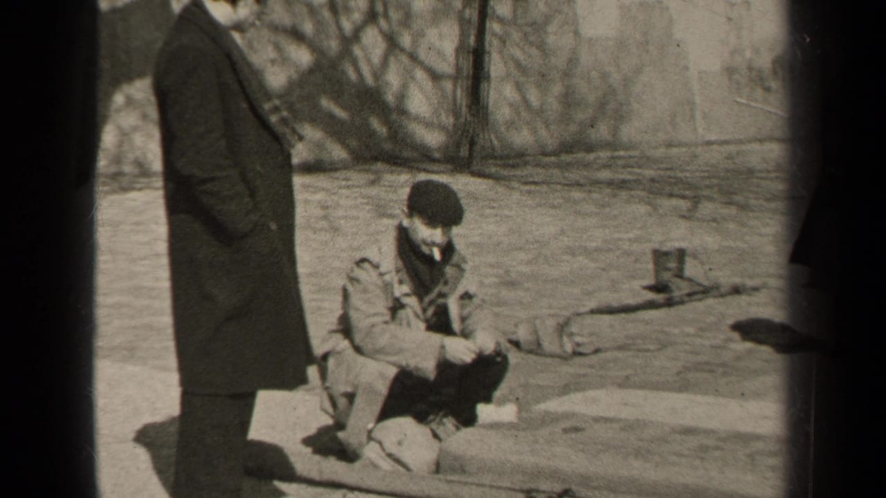 In the Paris home-movie scene, a man stands at left while another crouches on a ledge with a cigarette, framed by bare branches and pavement.