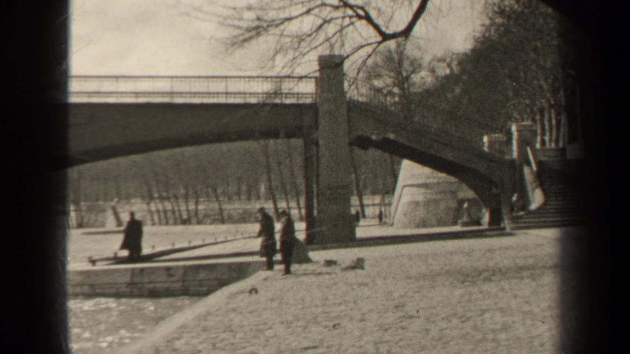 1947 Paris riverbank view with a stone bridge, pedestrians on the embankment, bare trees, and soft black-and-white 8mm texture.