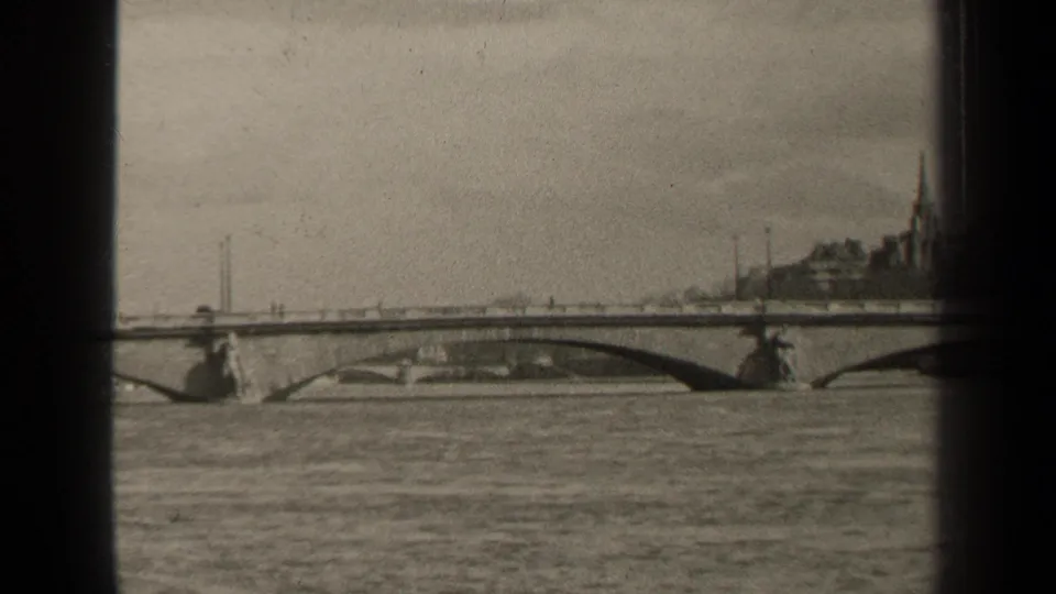 Black-and-white Paris river scene showing an arched bridge across the water, distant buildings, a church spire, and small figures on the bridge.