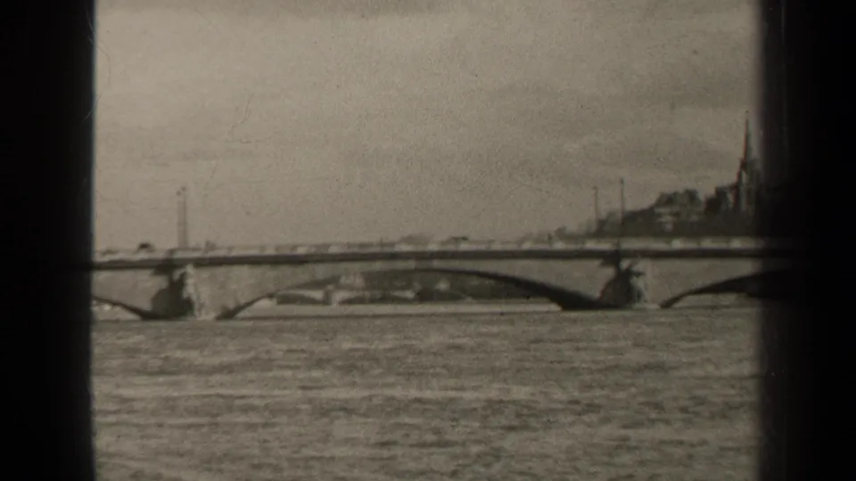 Paris river view in 1947 with a low arched bridge, distant urban skyline, church spire, and visible 8mm frame edges.