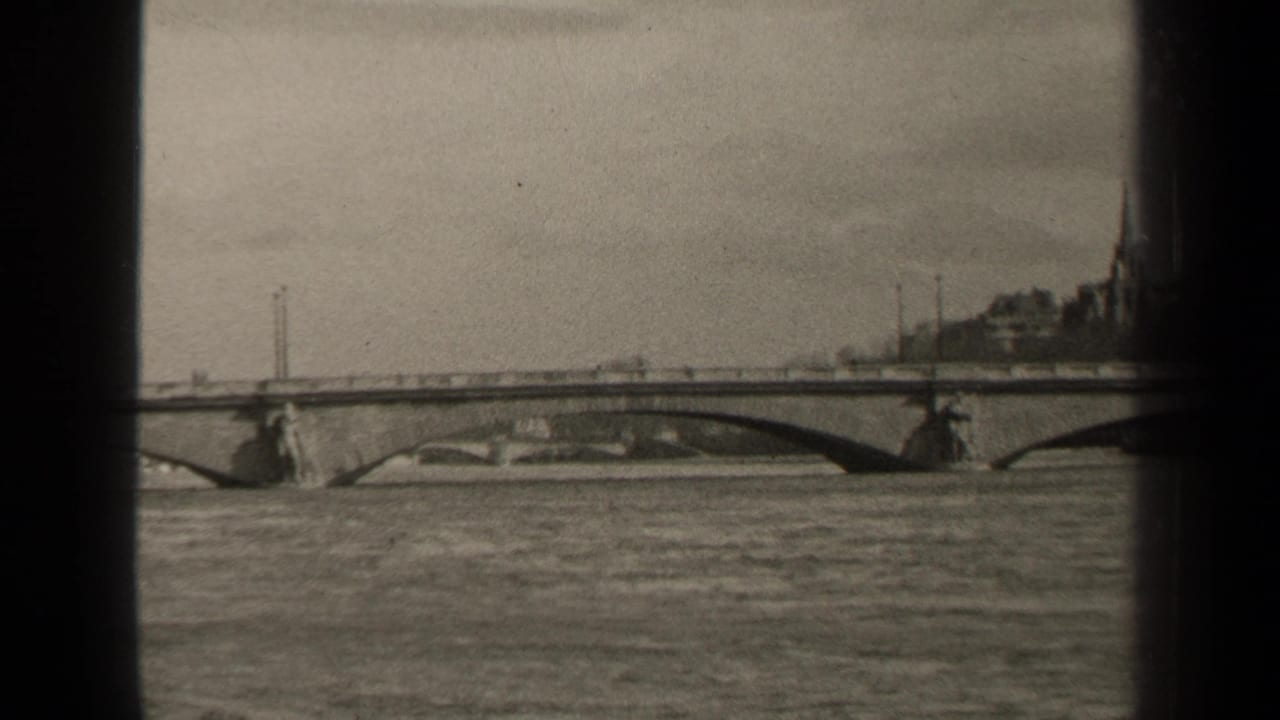 1947 Paris home-movie frame showing an arched bridge across a broad river, with distant buildings and heavy 8mm frame borders.