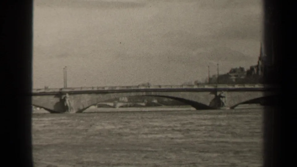 1947 Paris home-movie frame showing an arched bridge across a broad river, with distant buildings and heavy 8mm frame borders.
